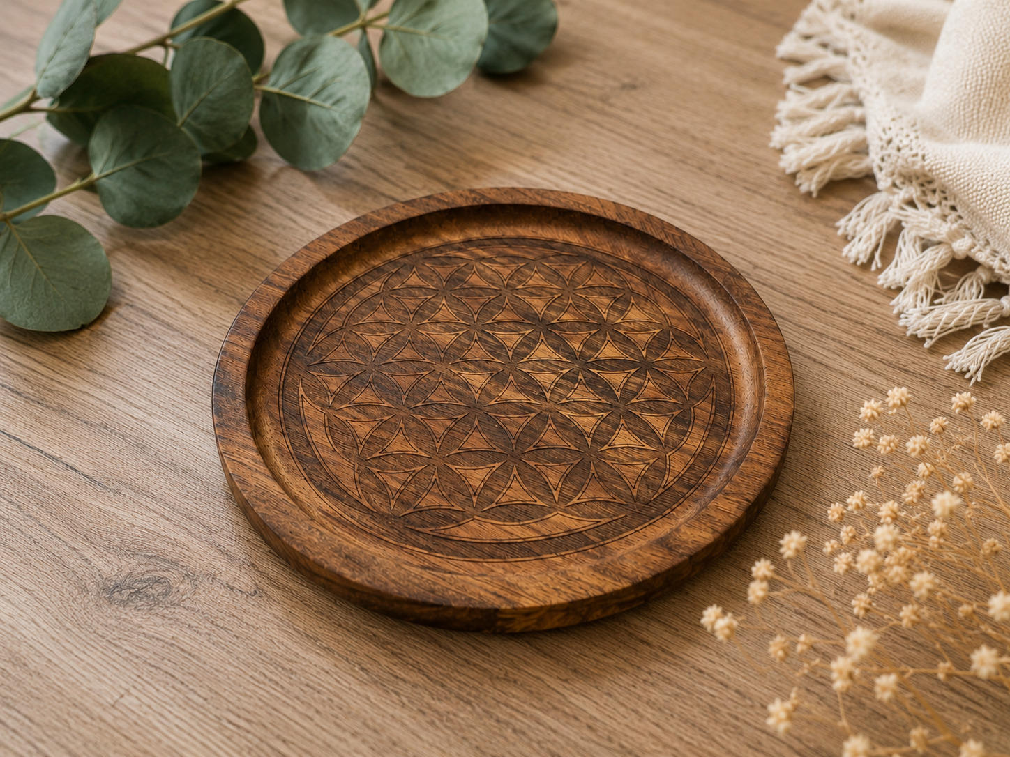 Plateau décoratif en bois gravé du motif Fleur de Vie, photographié en perspective sur une table en bois avec une décoration végétale minimaliste.